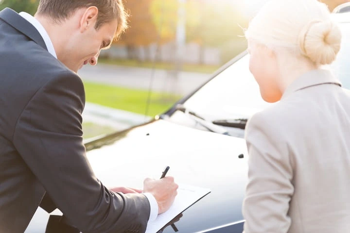 homme signant un document sur le capot d'une voiture avec une femme à sa droite