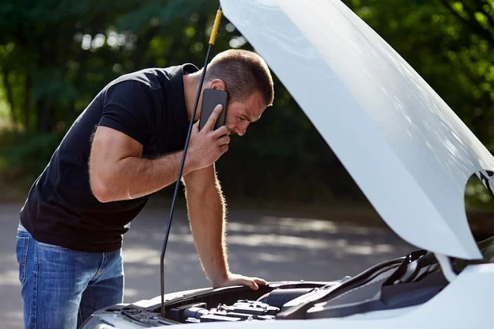 homme au téléphone avec le capot de sa voiture ouvert